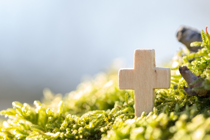 Holzkreuz im Grünen vor blauem Himmel