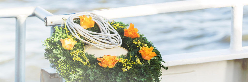 Blumenkranz und Urne auf einem Boot als Symbol für Bestattungsarten ohne Kirche