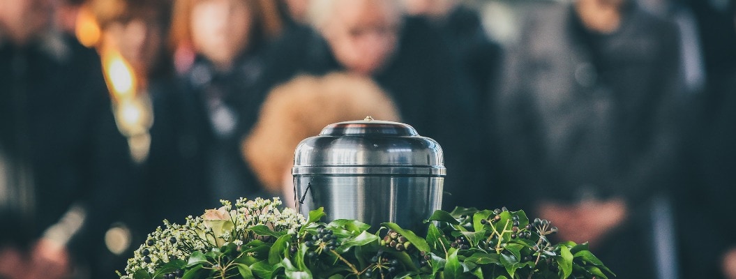 Eine Metallurne mit der Asche eines Verstorbenen auf einer Beerdigung, mit trauernden Menschen im Hintergrund auf einer Gedenkfeier. Trauriger Moment am Ende eines Lebens. Letzter Abschied von einer Person in einer Urne.